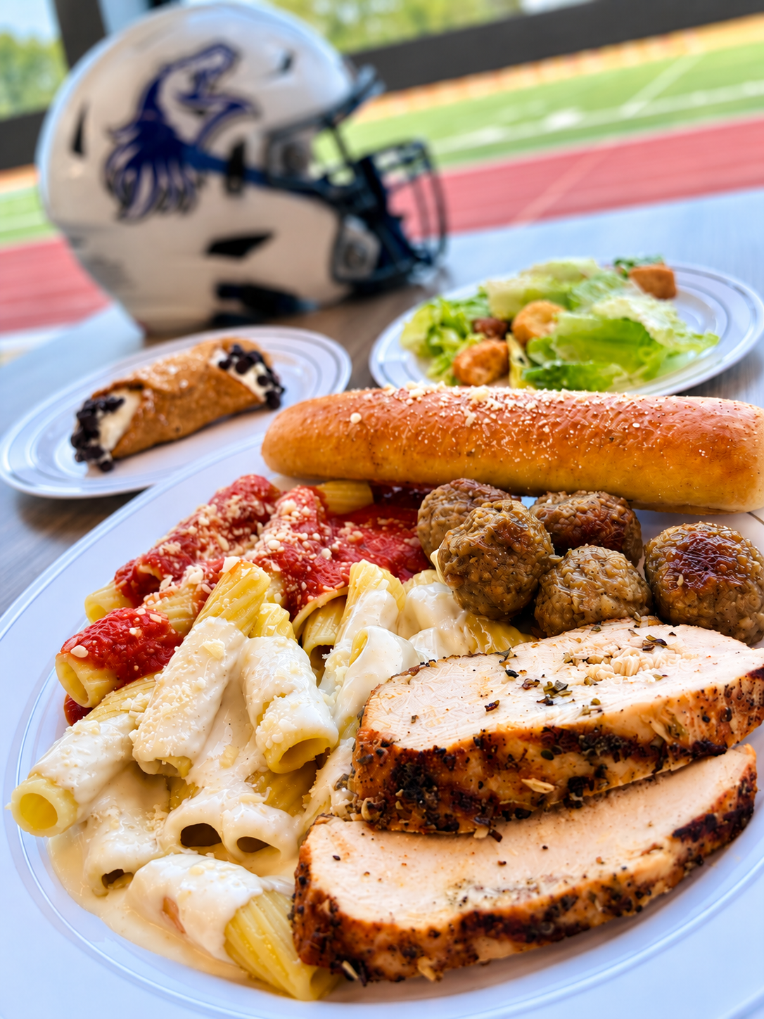 Luna Mesa Catering Italian spread with rigatoni, sliced chicken, meatballs, garlic bread, Caesar salad and cannoli at a stadium event